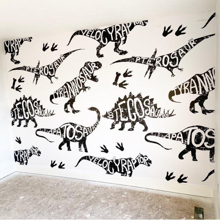 Bold dinosaur wall mural featuring oversized illustrated dinosaurs with their names incorporated as lettering, available in peel and stick or removable pre-pasted wallpaper.