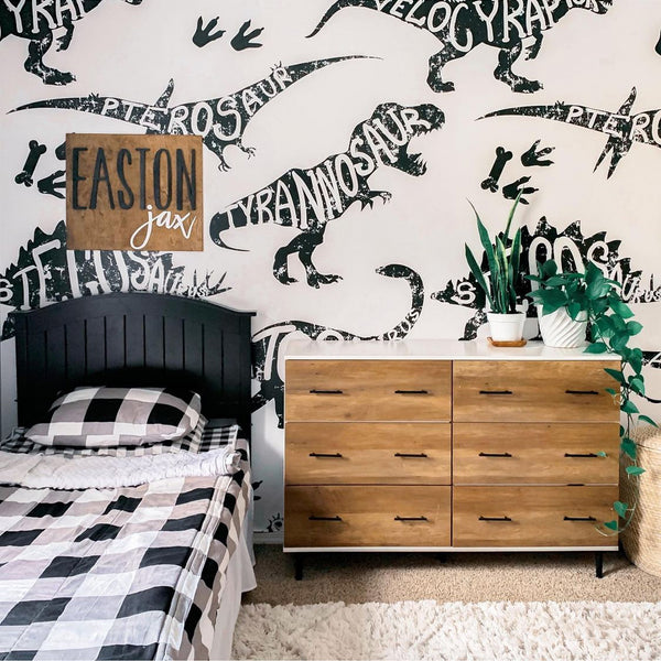 Black and white dinosaur mural wallpaper featuring oversized T-Rex, Velociraptor, Stegosaurus and other dinosaurs with typography-style names built into each shape.