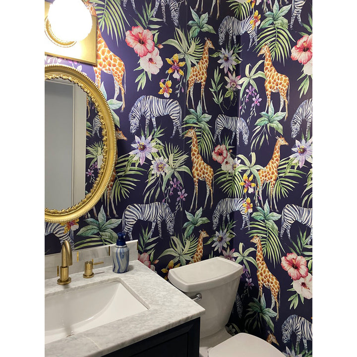 Vibrant safari wallpaper design with tropical flora, giraffes, and zebras, printed in vivid colors on a navy base, available as peel and stick or pre-pasted for effortless installation.